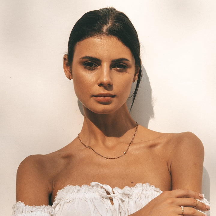 A woman in white dress wearing Roucou hoops earrings and Khasi necklace by Sceona fine jewellery